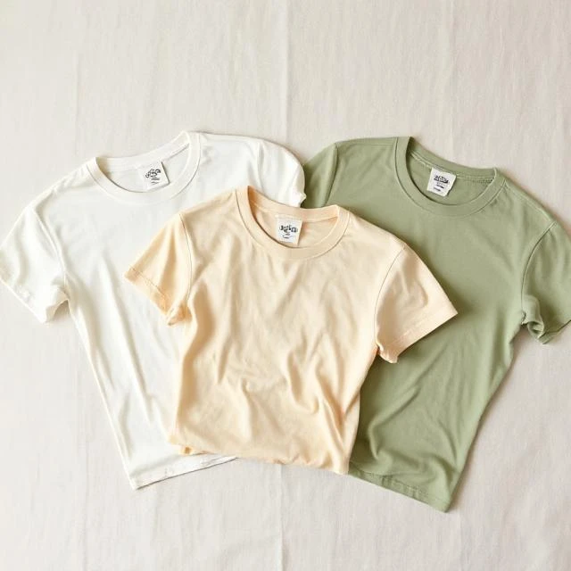 Flat lay of organic cotton T-shirts in off-white, sand and sage green colors with eco paper hangtags - sustainable T-shirt manufacturer Tiruppur India.